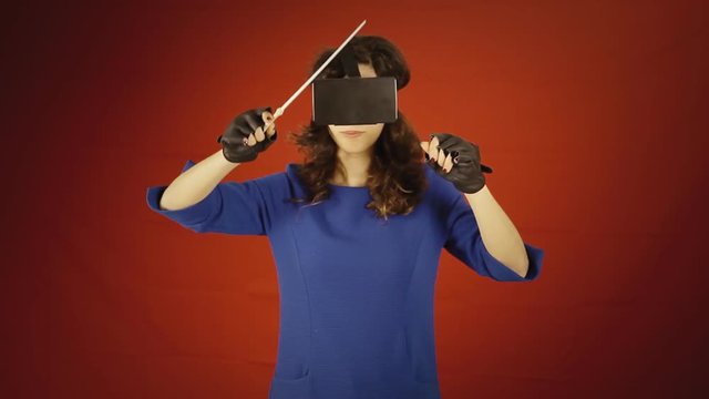 A young woman wearing a virtual reality headset and wired gloves, directing an orchestra with visible gestures of a baton, thanking the audience.
