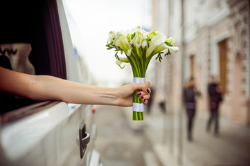 Bride's hand with a bouquet leaned out of the car