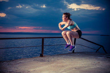 Strong young woman doing plyometric exercises on pier