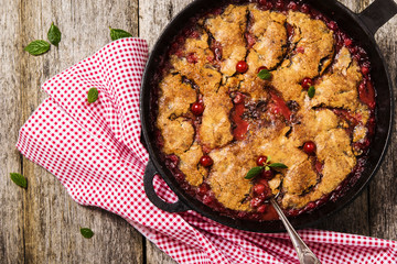 Cherry, cinnamon and chocolate cobbler on rough worn boards with cloth and leaves of cherry 