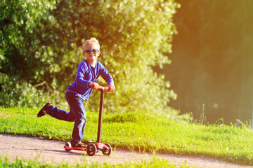 little boy riding scooter in summer