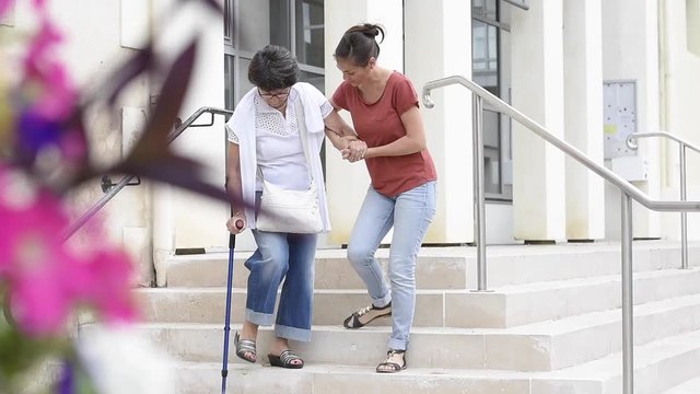 Home carer helping disabled woman getting down the stairs
