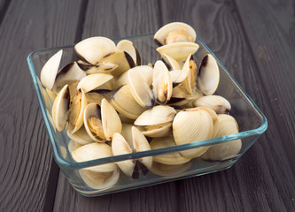 glass saucepan, filled with uncooked clams on wooden