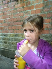 Girl drinking orange juice against a brick wall