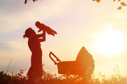 Silhouette Of Mother With Little Baby And Stroller At Sky