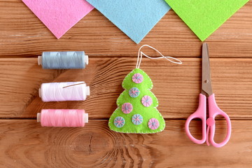 Green felt Christmas tree with pink and blue circles, thread, scissors, needle on a wooden table. Hanging ornament Christmas tree. Kindergarten, preschool and elementary school craft. Top view