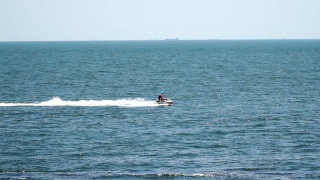 Jetski on the sea pulls inflatable mattress. On the mattress there are people. On the horizon are visible ships. Slow motion,high speed camera