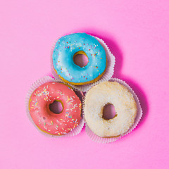 three colorful round donuts on pink background