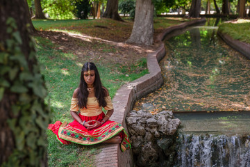 Young beautiful traditional indian woman practicing yoga in natu
