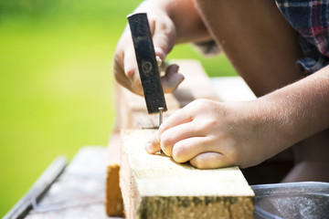 Fototapeta na wymiar Boy learns to hammer nails in a garden