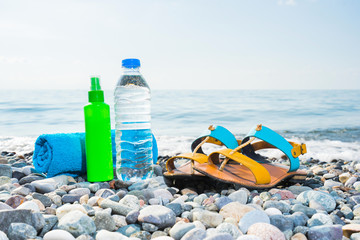 Vacation concept. Essentials on the sea beach. Bottle of drinking water,  towel,  woman shoes and sun protected cream.