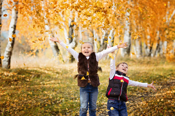 Fototapeta premium Laughing brother and sister throw up leaves in the autumn forest