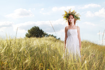 девушка с венком в поле одета в белое платье