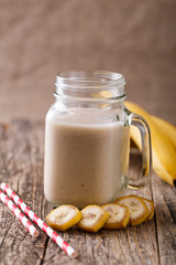 Healthy banana smoothie in glass jar with bananas on wooden tabl