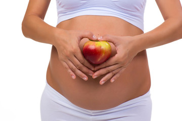 Close-up of a pregnant belly and apple. Hands folded heart. On a white background