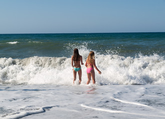 Two young girls standing in the sea-wave on the beach in Chania. Crete island, Greece