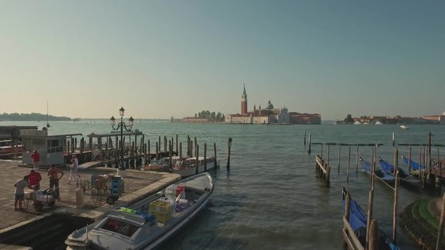 VENICE, ITALY - JUNE 19, 2016: Parking gandolas on the Doge's palace embankment with the bell tower of the Saint Giorgio Maggiore church view, Venice, Italy.