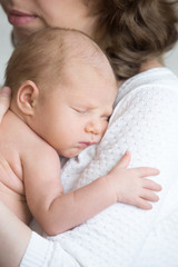 Portrait of young mother tenderly embracing sleeping cute new born child. Funny newborn babe napping in mom arms. Mum and healthy little kid. Love, bonding, happy family concept