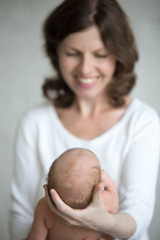 Young happy mother holding her sleeping newborn cute babe. Newborn babe resting in mom hands. Healthy little kid after birth lying in parent arms. Month old baby. Focus on infant head. Closeup