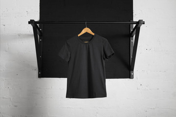 Blank black t-shirt presented on wooden hang on pullbar in home gym
