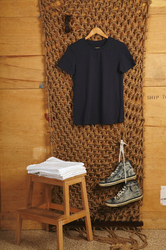 Black basic cotton t-shirt presented in rustic interior, white folded shirts on small wooden stairs below