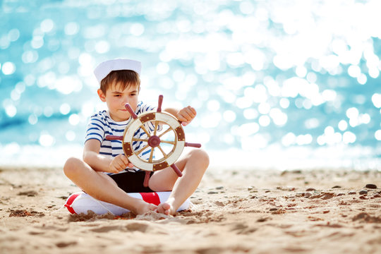 seven years old boy playing at the beach in sailor hat. Child with a steering wheel at sea