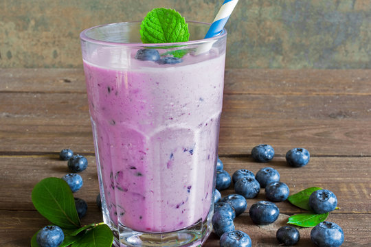 blueberry smoothie in a glass with a straw, mint and fresh berries