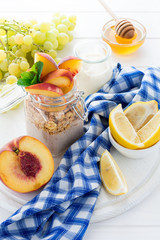 Healthy breakfast: muesli with smoothie, honey, yogurt and fresh berries in a glass jar on white wooden background