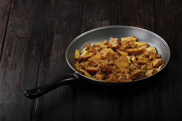 fried meat in frying pan on wooden background