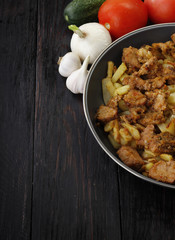 fried meat and potato with vegetables on wooden background