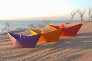 Three paper boats on a beach at sunrise