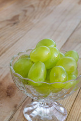 Green grapes in the crystal glass bowl on the wooden background