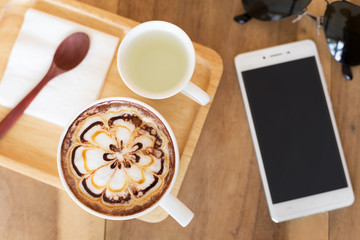 A cup of coffee with flower latte art on top and bread heart and Sunglasses.