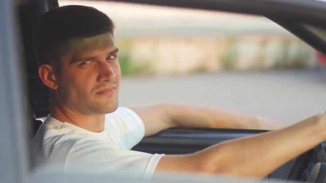 portrait of a young man behing the wheel looks at camera, slow-motion