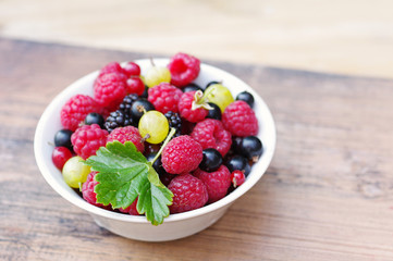Fresh juicy berries, raspberries, currants, blackberries, a gooseberry in an white plate on a wooden surface