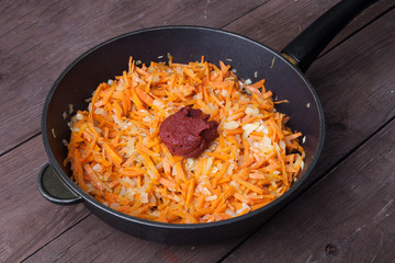 Chopped carrots and onions with tomatoes paste in a frying pan f