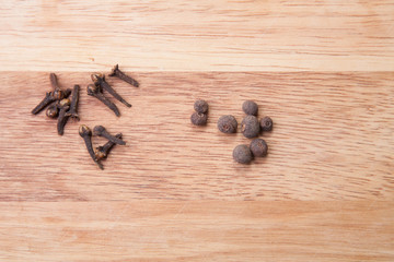Cloves and black pepper on light wooden cutting board