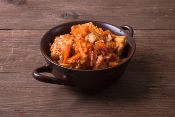 Fish marinated with carrots in a brown ceramic bowl on old woode