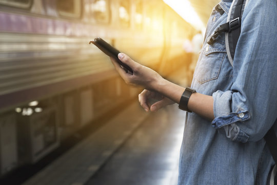 woman holding smartphone with backpack at train station