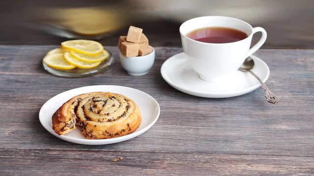 Steaming black tea, brown sugar, lemon and sweet roll cakes with poppy served on a wooden tableagainst steel kitchen background
