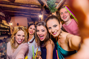 Young beautiful people with cocktails in bar taking selfie