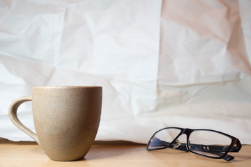 Coffee mug and glasses on the wooden table with the crumpled paper as background