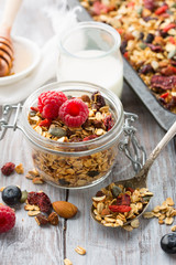 Fresh granola, muesli with berries, honey in a glass jars on a white wooden background, selective focus