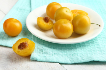 Yellow plums lying on a plate on wooden white background.