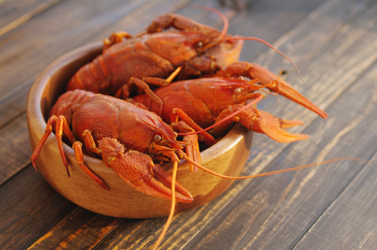 Boiled crawfishes in a round wooden plate on a wooden background, close up