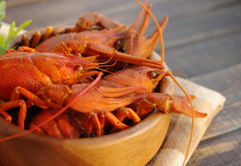 Boiled crawfishes in a round wooden plate on a wooden background, close up