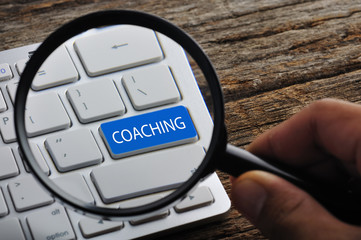Hand Holding Magnifying Glass with "COACHING" Word On Keyboard