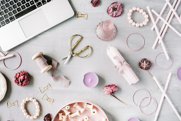 Flat lay, top view office table desk. Workspace with laptop, purple candles, spool set, decor, golden scissors and clips on grey concrete background.