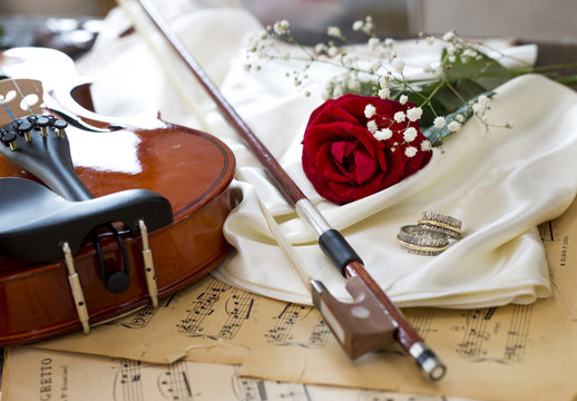 Violin, red rose, marriage rings, wine and music notes on satin fabric
