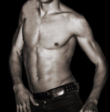 Sexy young male in jeans showing abs on black background. Image black and white.